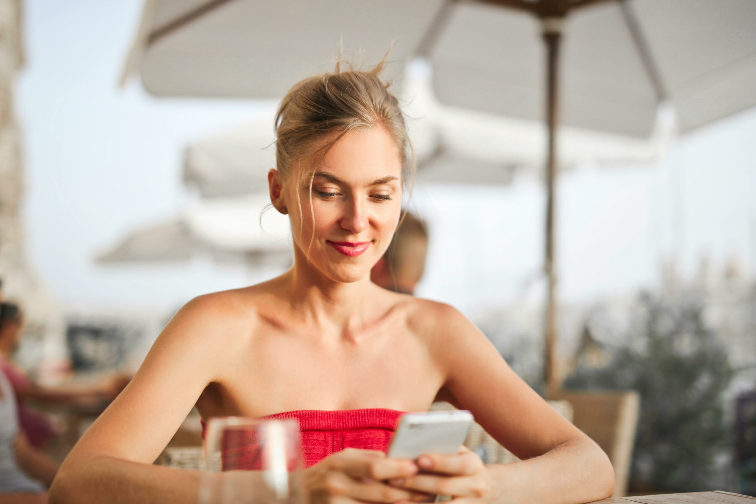 image of an attractive blonde woman looking at her cell phone with a smile on her face communicating the ease how to create a personal budget in 3 simple steps