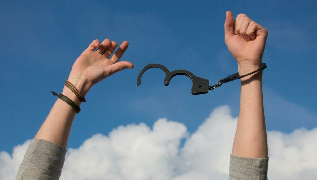 with blue skies and puffy white clouds in the background a pair of hands is breaking free from a pair of handcuffs, a perfect symbol for Strategies For Paying Off Credit Card Debt